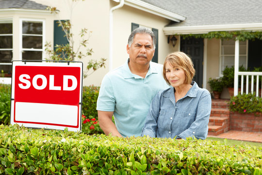 Senior Hispanic Couple Outside House With Sold Sign