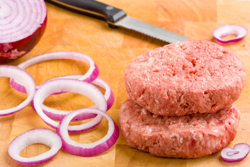 Raw beef burgers and red onion on chopping board.