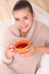 Female is drinking a tea in an orange cup.