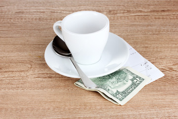 Empty cup of coffee with five dollars tip on wooden background
