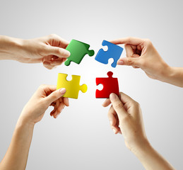 Hands and puzzle on gray background. Teamwork solving a puzzle - obrazy, fototapety, plakaty
