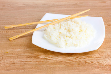 White bowl of cooked rice and chopsticks on wooden table
