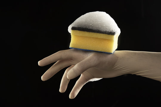 mano con guante de latex con esponja con jab&oacute;n en fondo negro