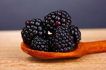beautiful blackberries in wooden spoon on gray background