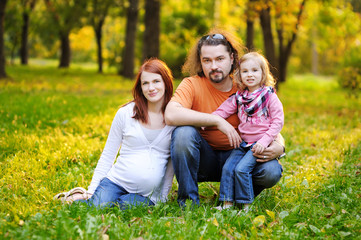 Fototapeta premium Beautiful expecting family in autumn park at sunset