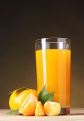 Tangerines and juice glass on wooden table on brown background