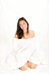 Schöne junge Frau sitzt auf weißem Bett