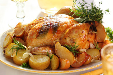 Whole roasted chicken with potatoes and apples on white plate