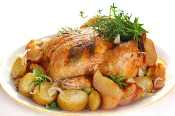 Whole roasted chicken with potatoes and herbs on white plate