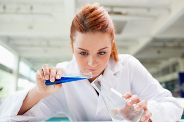 Beautiful serious scientist pouring liquid