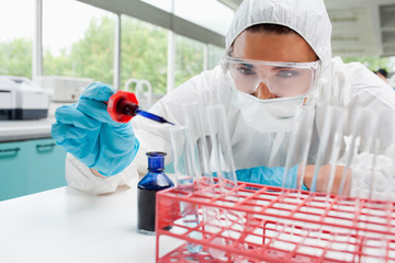 Protected cute female scientist dropping blue liquid in a test t