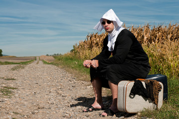 homme déguisé en none assis sur une valise au bord d'un chemin