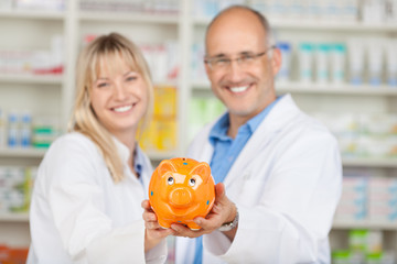 zwei kollegen in der apotheke präsentieren sparschwein