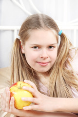 beautiful girl sits in bed and holds a ripe apple in a hand