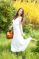Beautiful girl with bast basket and apples on the nature