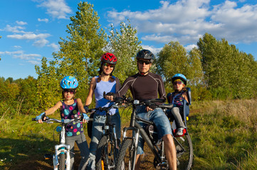 Naklejka na ściany i meble Family cycling outdoors. Happy parents with two kids on bikes
