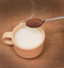 Taza de leche y cucharilla con café instantáneo.