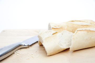 Baguette and bread knife on chopping board isolated on white