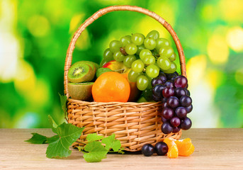 Ripe juicy fruits in basket on wooden table on green background