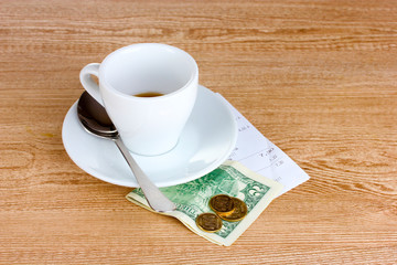 Empty cup of coffee with five dollars tip on wooden background