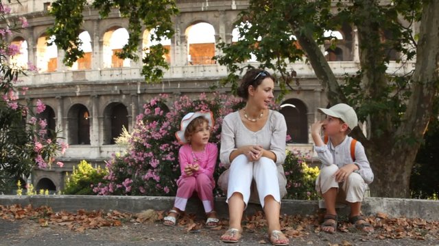 Woman tells story to girl and boy sit in front of Colosseum