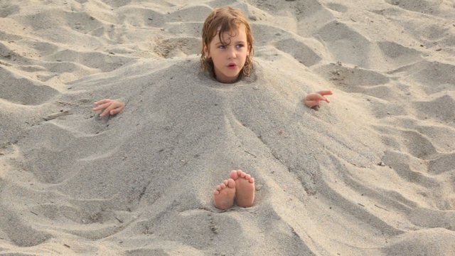 Little girl sits filled up with sand on neck on beach