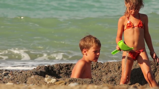 Two children are in a small pit in sand before water