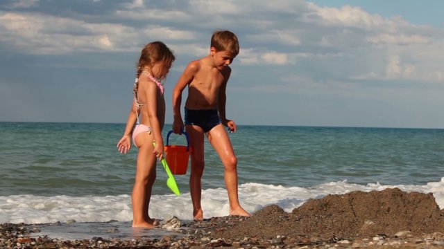 Two children are in small pit in sand before water