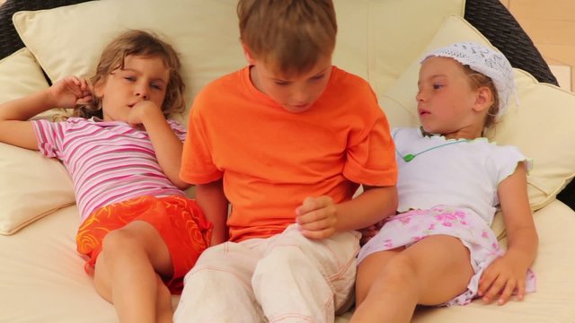 Three children lying on pillows on bed and talking