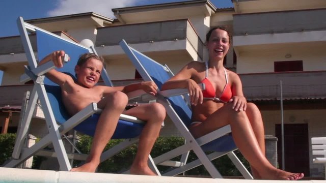 Mother and her son sitting in deckchairs at pool edge