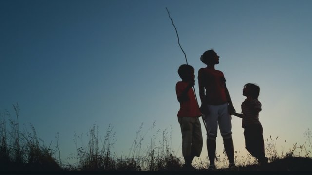 Mother and kids standing on hill, boy holding long thin stick