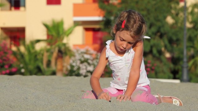 Little girl sitting on sand and writing on it