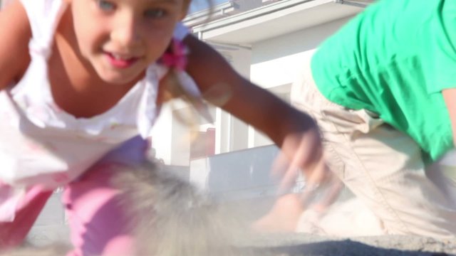 Two kids grabble by sand kicking up dust