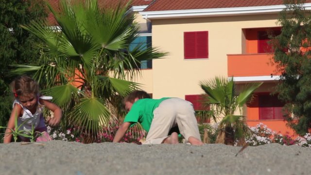 Two kids grabble by sand kicking up dust