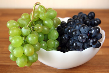 fresh white and red grapes in white bowl on wooden table