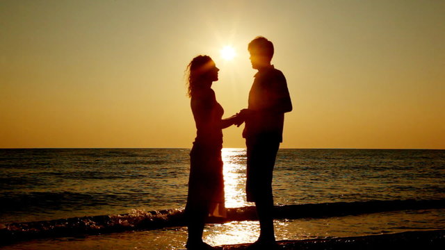 Boy and girl standing on beach, silhouettes at sunset, part2