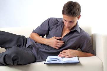 Fototapeta premium Young man reading book on the sofa at home