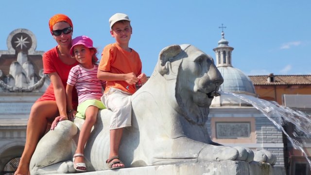 Mother and her kids sit on statue of lion near Flaminio obelisk