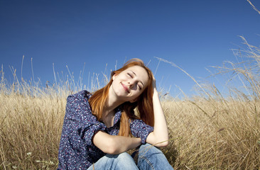 Portrait of happy red-haired girl on autumn grass.