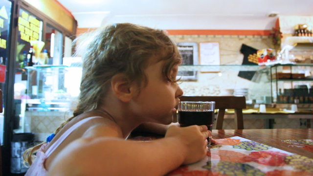Little girl sits at table and drink from glasses