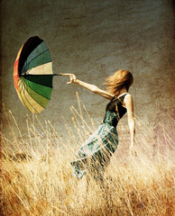 Redhead girl with umbrella at windy grass meadow.