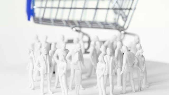Little toy men and women stand in front of big shopping trolley