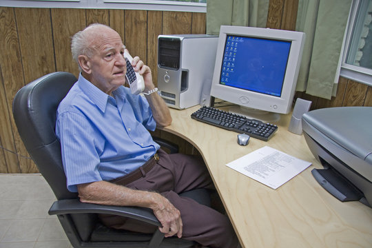 Senior Talks On Phone At Computer Desk