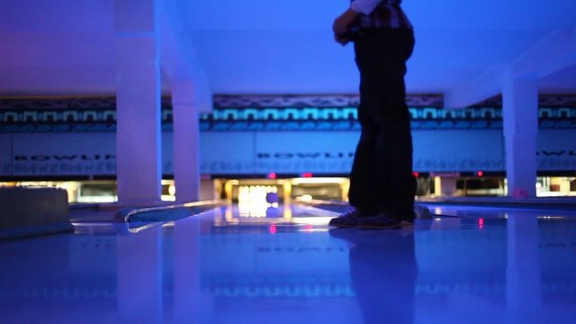 Boy throws ball in illuminated bowling club