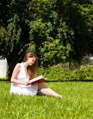 Girl-student sit on lawn and reads textbook