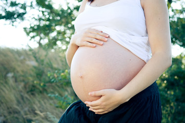 Pregnant woman in nature holding her belly