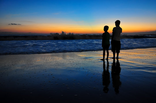 Two boys at ocean coast at sunset