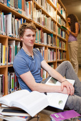 Portrait of a male student with books while his classmate is rea