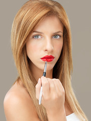 young blonde woman applying red lipstick brush