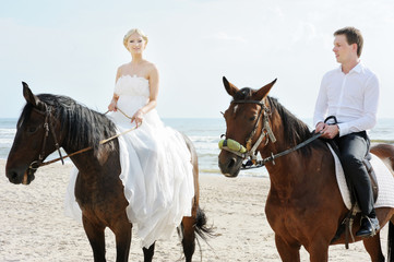 Beach wedding: bride and groom on a horses by the sea